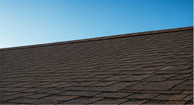 Brown shingle roof against a clear blue sky. The roof's linear pattern is prominent, creating a simple and calm scene. No text visible.
